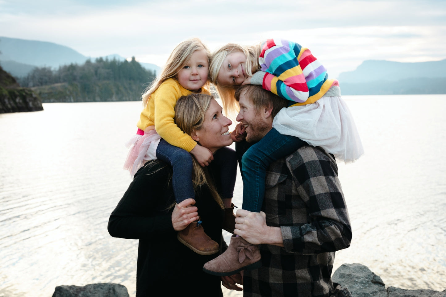 Family of four with two children on shoulders by a body of water. Minimalist portrait mini session, Hood River Oregon photographer