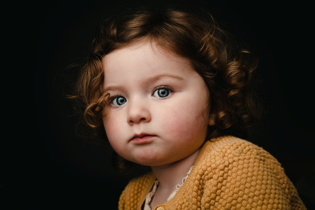 Child wearing a yellow sweater against a dark background. Minimalist portrait mini session, Hood River Oregon photographer