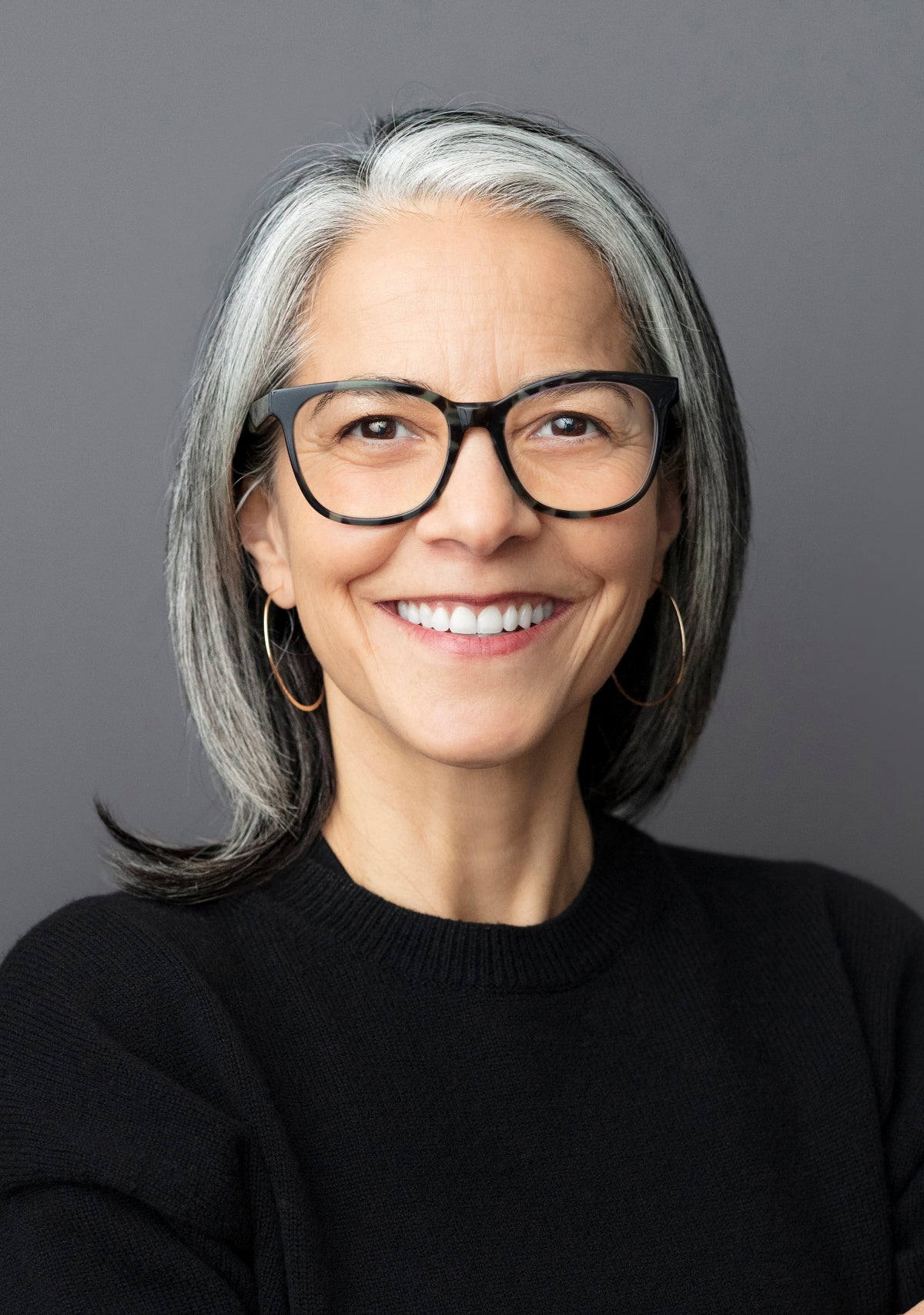 Woman with gray hair wearing black glasses and a black sweater against a gray background. Hood River Oregon photographer