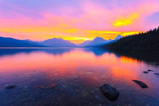 Glacier National Park at sunrise with vibrant pink, purple, and yellow in the sky and with mountain peaks in the background - fine art landscape photography print