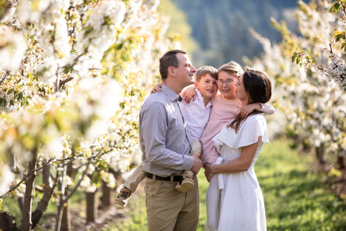 Family of four posing for a photo in a blossoming orchard.  Spring blossom mini portrait session, Hood River Oregon 