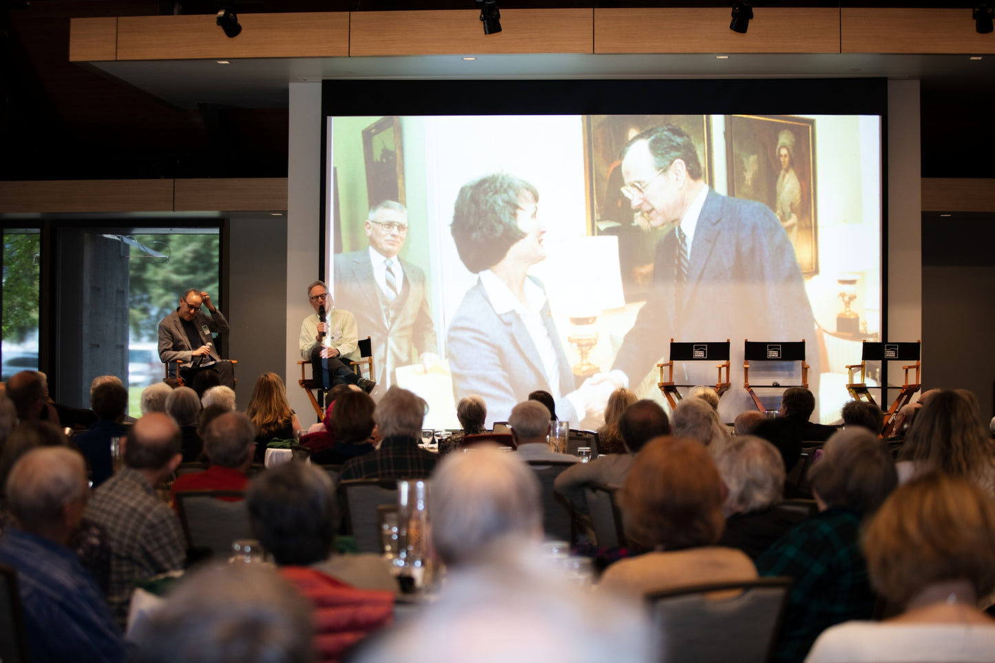 Audience watching a presentation with a large screen displaying images of people. Event photographer at Columbia River Gorge, Oregon