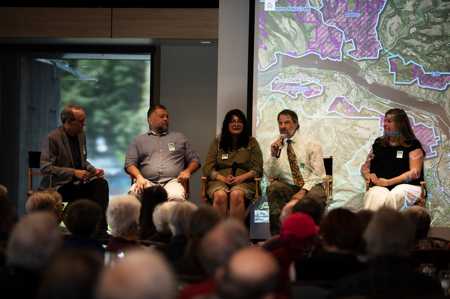 Panel discussion with four speakers on a stage in front of an audience, with a map displayed on a screen behind them. Event photographer at Columbia River Gorge, Oregon